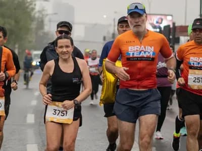 Un grupo de corredores avanza por una avenida en un día nublado; varios llevan polera del Brain Team y su número.