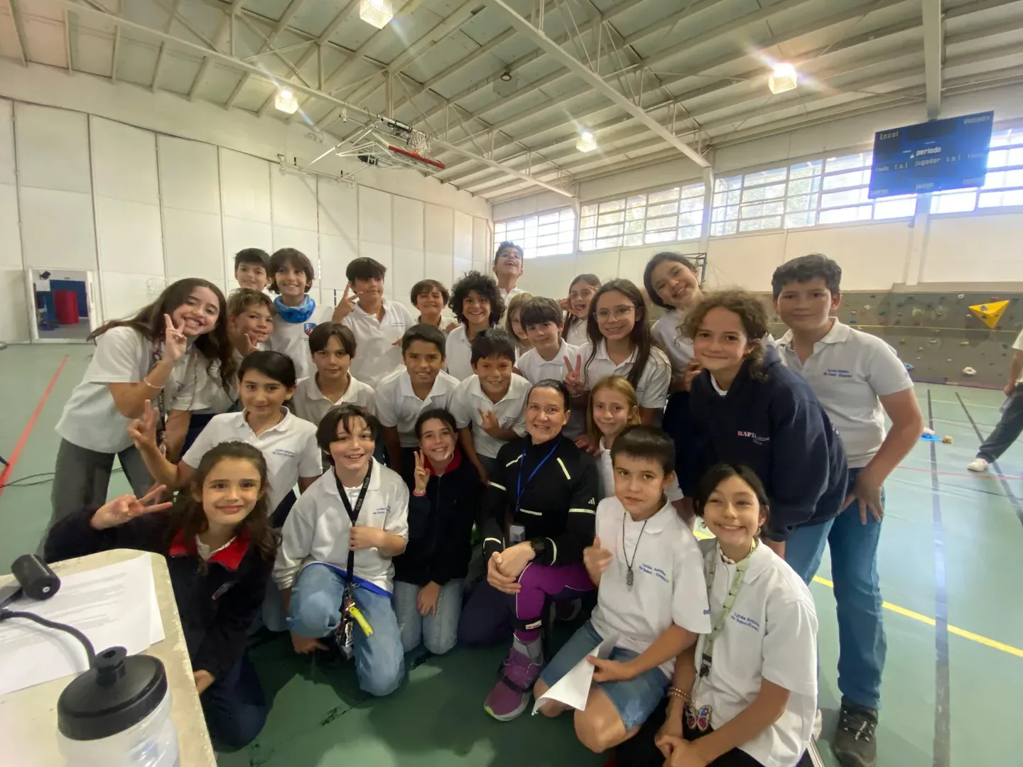 Macarena Larraín rodeada de un grupo grande de estudiantes de básica en el gimnasio, posando y sonriendo al terminar la actividad.