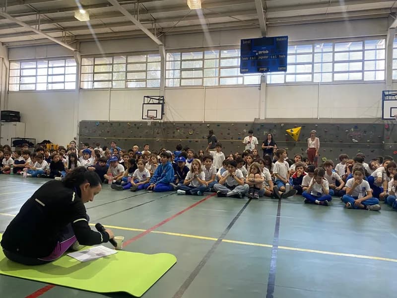 Macarena Larraín, sentada sobre una colchoneta, habla a los estudiantes reunidos en el suelo del gimnasio.