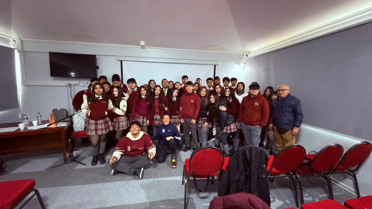 Macarena Larraín, arrodillada al frente y con el puño en alto, rodeada por los estudiantes del área técnico profesional en el auditorio del colegio.