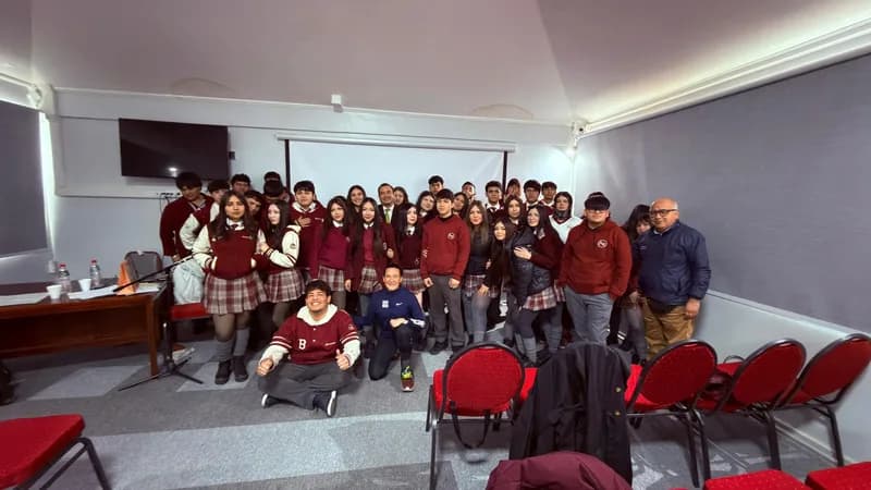 Vista general del auditorio al terminar la charla: el curso posa de pie junto a Macarena Larraín y sus profesores, frente a la pantalla.