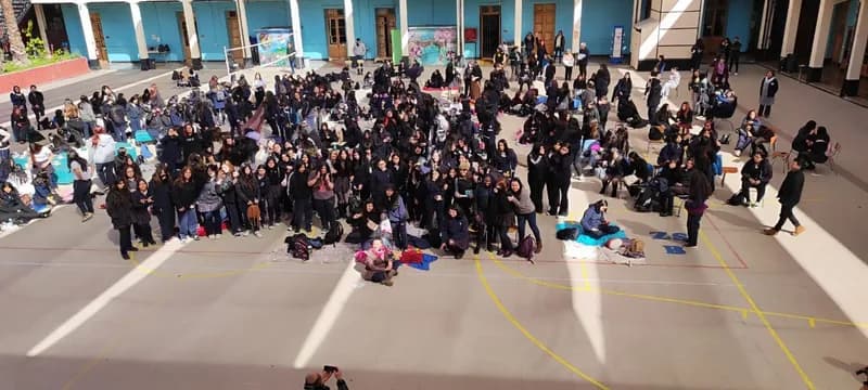 Vista desde arriba del patio lleno de estudiantes con uniforme, reunidas y sentadas en el suelo durante la actividad.