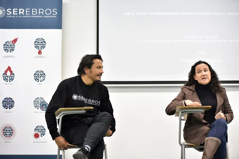 Macarena Larraín responde una pregunta mientras el moderador la escucha. A la izquierda, el pendón de SEREBROS con los tipos de lesión cerebral adquirida.