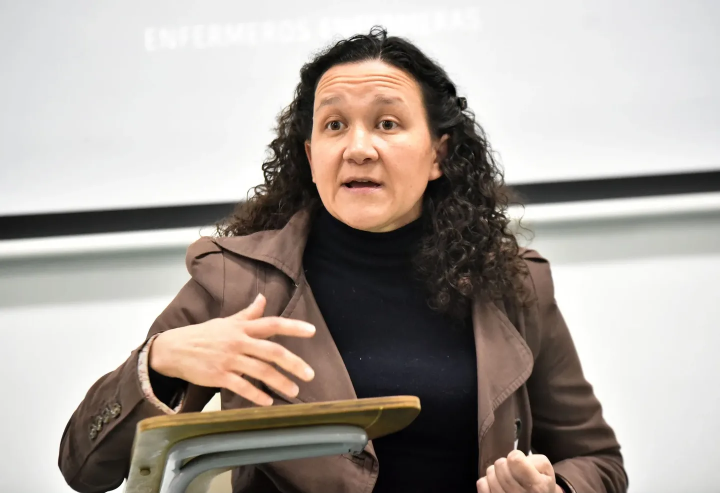 Macarena Larraín hablando frente al público, sentada en una sala de clases, con la proyección de los créditos del documental detrás.