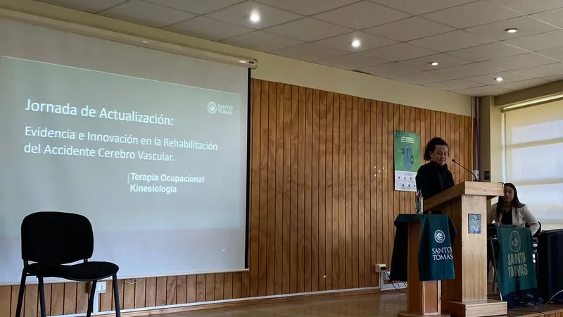 Plano abierto del auditorio de la Universidad Santo Tomás: el escenario, la pantalla con el título y el podio con pendones.