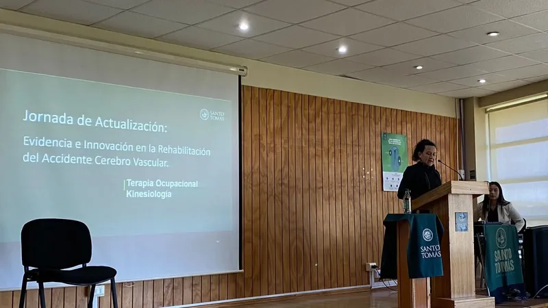La pantalla del auditorio anuncia la Jornada de Actualización sobre evidencia e innovación en la rehabilitación del accidente cerebrovascular, para Terapia Ocupacional y Kinesiología, mientras una expositora habla desde el podio.