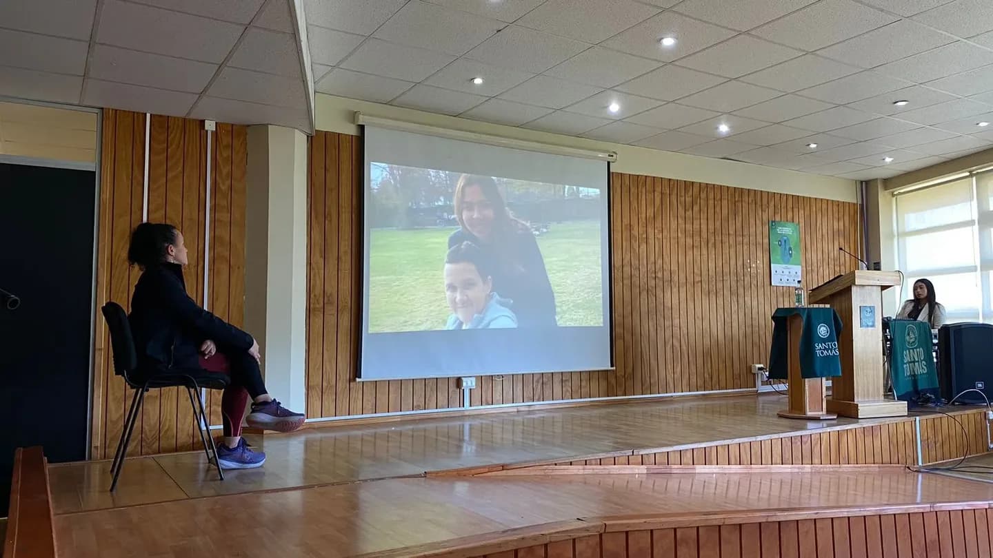 Macarena Larraín sentada al costado del escenario del auditorio, mirando la proyección de su documental.